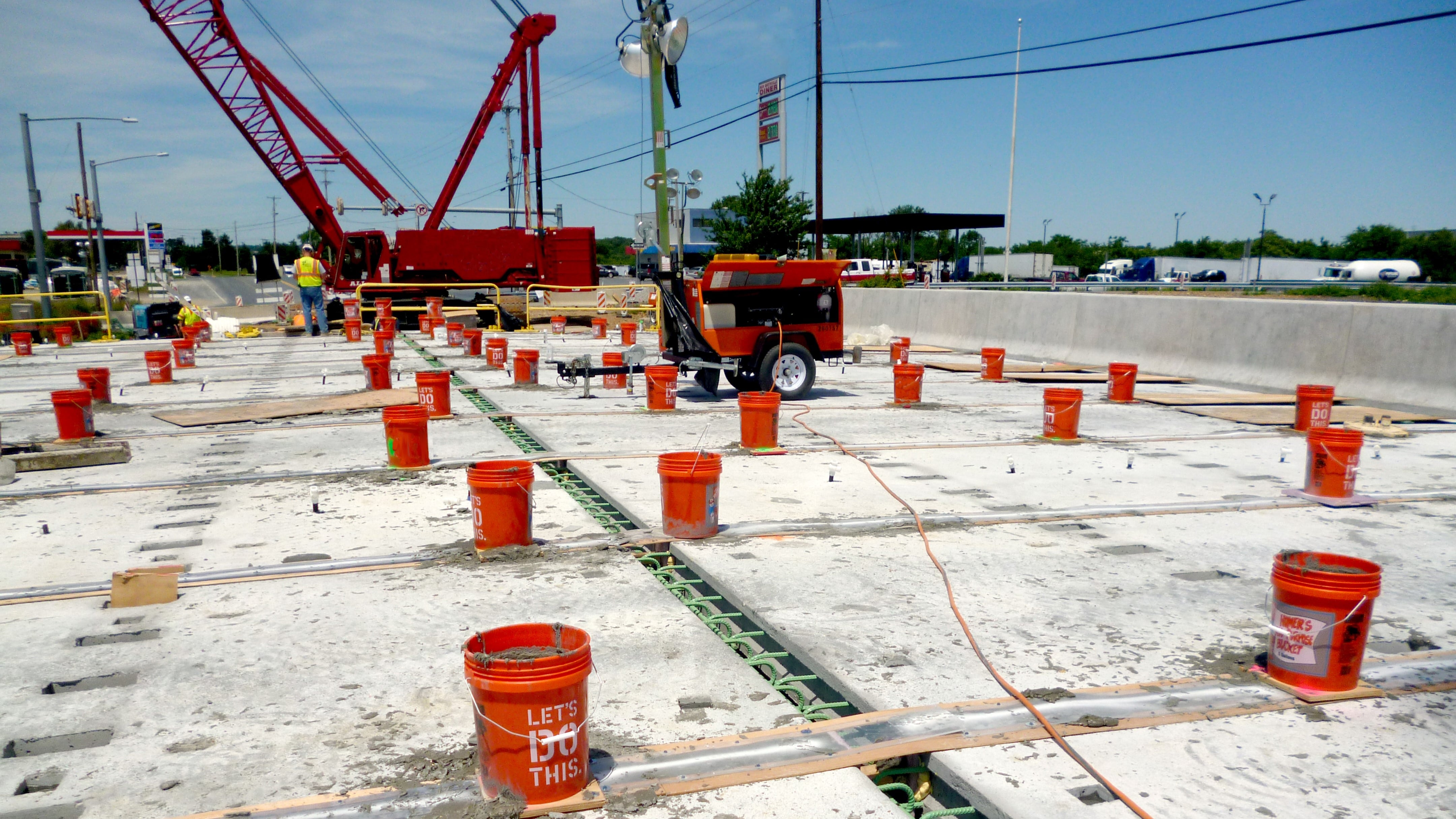 An image of a bridge deck lined with orange buckets in preparation for construction workers to apply Ultra-High Performance Concrete between prefabricated bridge elements